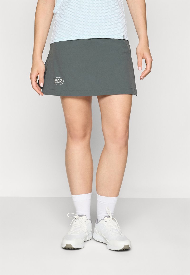 Dark gray sports skirt with a fitted design, featuring an EA7 logo on the side. The model wears white socks and sneakers.