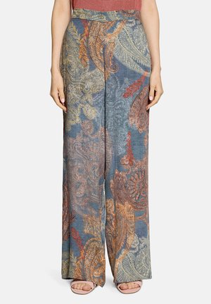 Wijde broek met blauw, oranje en beige paisleypatroon, gedragen met roze sandalen met open teen en een rood topje.