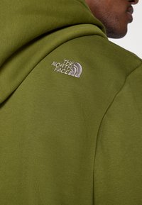 Φούτερ με κουκούλα σε ελιά πράσινο χρώμα, κατασκευασμένο από υφασμάτινη υφή, με λευκό κεντημένο  λογότυπο "The North Face" στον αριστερό ώμο.