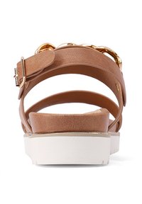 Sandalo in finta pelle marrone con una fascia ampia, dettaglio in catena dorata e suola bianca a piattaforma. Cinturino alla caviglia regolabile con chiusura a fibbia.