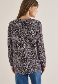 Langærmet bluse med et abstrakt mønster i lilla og hvid, med rund halsudskæring og rynkedetalje bagpå. Blødt stoftekstur.