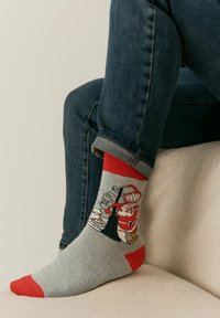 Gray and red socks feature a cartoon design of a character by a snowman, with a textured knit and colored toe and cuff accents.