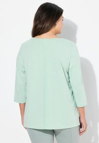 Mentolově zelený, lehký top se třemi čtvrtinovými rukávy, rovně sešitou zadní částí a zaobleným výstřihem. Měkká textura a uvolněný střih.