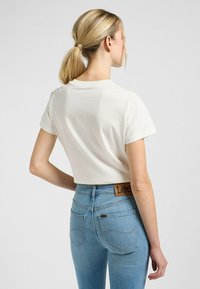 Hvid cropped t-shirt med korte ærmer, parret med lyseblå højtaljede jeans med et læderbælteskilt og baglommer.