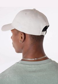 Casquette de baseball gris clair avec une visière incurvée, une sangle arrière ajustable et un logo blanc. Portée avec une chemise verte et un collier en chaîne argenté.