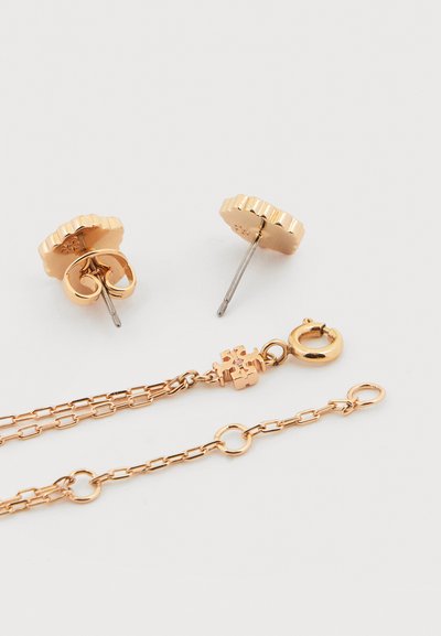 Σκουλαρίκια με καρφάκι σε χρυσό τόνο με κυματιστές άκρες και ασορτί κολιέ αλυσίδας με κούμπωμα κλωβού και διακοσμητική λεπτομέρεια με τετράγωνους κρίκους.