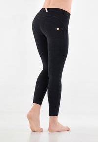 Leggings neri con design a vita alta, texture liscia, cuciture curve e due tasche posteriori con un accento di logo discreto.
