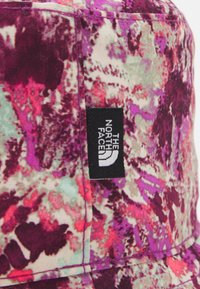 Flerfärgad tygbucket-hatt med blommönster i nyanser av lila, rosa och grön. "The North Face"-logotags synlig på sidan.