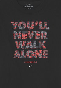 Svart Nike-t-shirt med mönstrad text "DU KOMMER ALDRIG ATT GÅ ENSAM" i röd och grå, Liverpool F.C. logotyp nedan med vit Nike-swoosh.