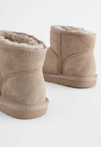 Kurze braune Wildleder-Stiefeletten mit samtiger Innenauskleidung, runder Form und flacher Gummisohle, ausgestattet mit gesteppten Details entlang der Nähte.