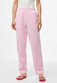 Roze sweatpants met een elastische tailleband en een recht gesneden ontwerp, gemaakt van zachte stof. Gekoppeld aan rode slippers.