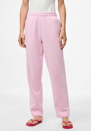 Pantalons de jogging roses avec une taille élastique et une coupe droite, fabriqués en tissu doux. Associés à des tongs rouges.