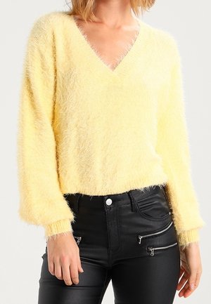 Person wearing a soft, fuzzy yellow V-neck sweater paired with high-waisted black pants featuring multiple front zippers.