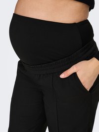 Musta äitiysfarkut joustavalla vyötärönauhalla, joissa on sileä pinta ja sivutaskut. Malli mukautuu kasvavalle vatsalle.