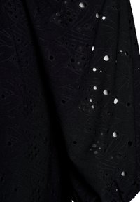 Tessuto nero con ricami dettagliati e fori a forma di fiore, texture liscia e cadente morbido.