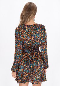 Rochie colorată cu mâneci lungi și talie ajustată, având un model abstract în nuanțe de portocaliu, teal și violet. Volan la tiv și detaliu cu fundiță la spate.