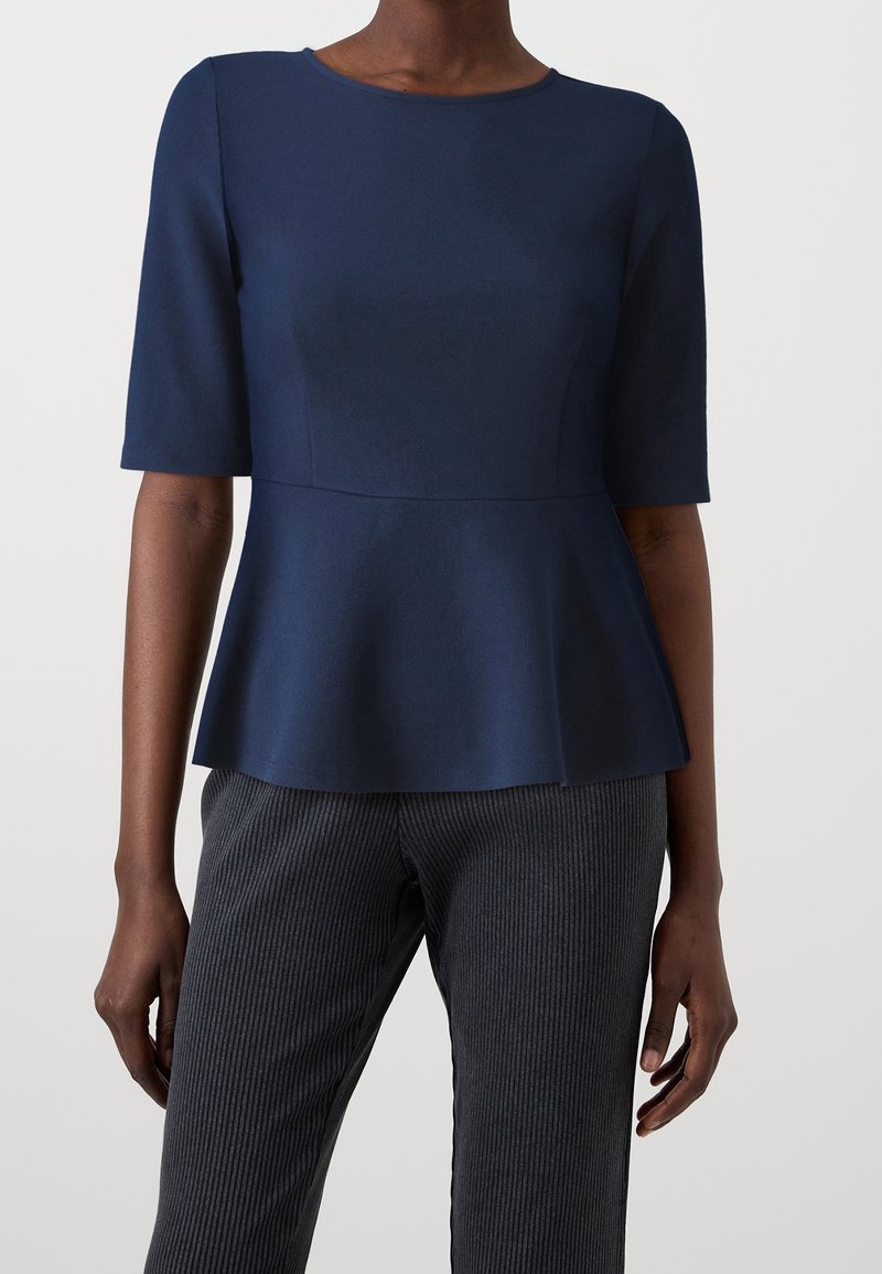 Haut péplum bleu marine à manches courtes, texture de tissu lisse, encolure ronde et corsage ajusté. Assorti à un pantalon tailleur rayé foncé.