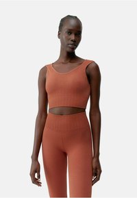 Roestkleurige crop top en bijpassende high-waisted leggings met ribbelstructuur. Heeft een ronde halslijn en een uitsnijding in de taille.
