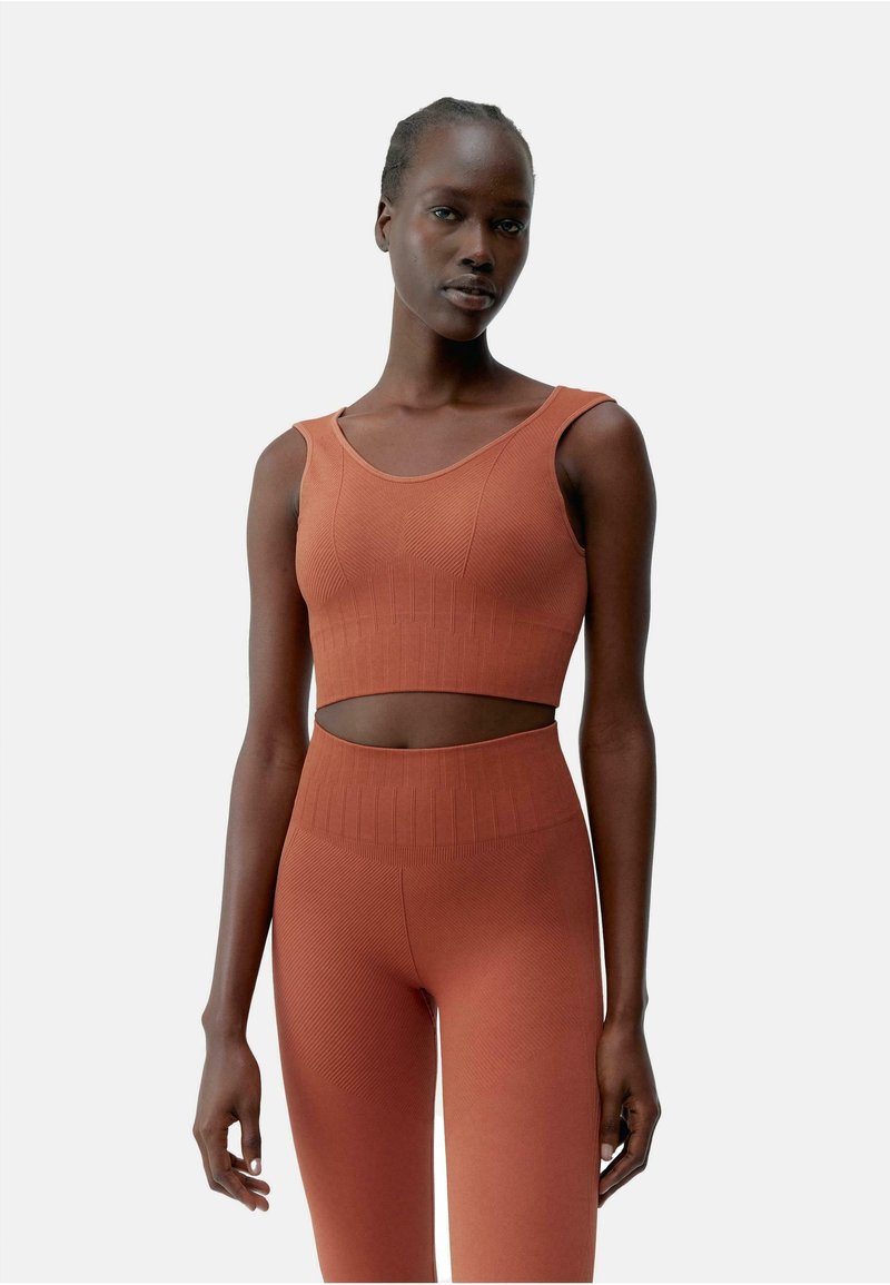Roestkleurige crop top en bijpassende high-waisted leggings met ribbelstructuur. Heeft een ronde halslijn en een uitsnijding in de taille.