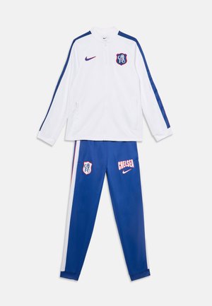 Бяло яке с цип с сини ивици и лого на Chelsea FC, съчетано със сини спортни панталони с надпис Chelsea и лого.