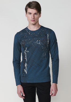 Camisa de manga larga azul marino con un diseño gráfico texturizado y acentos blancos. Presenta un cuello redondo y una silueta ajustada.