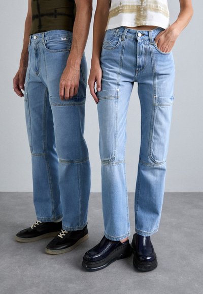 Light wash denim jeans with patchwork design and contrasting stitching. One pair features side pockets. Footwear includes black sneakers and platform shoes.