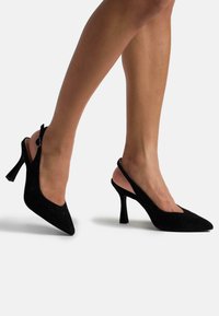 Décolleté slingback in suede nero con punta affusolata, tacco sottile e cinturino regolabile. Texture liscia e design minimalista con profilo elegante.
