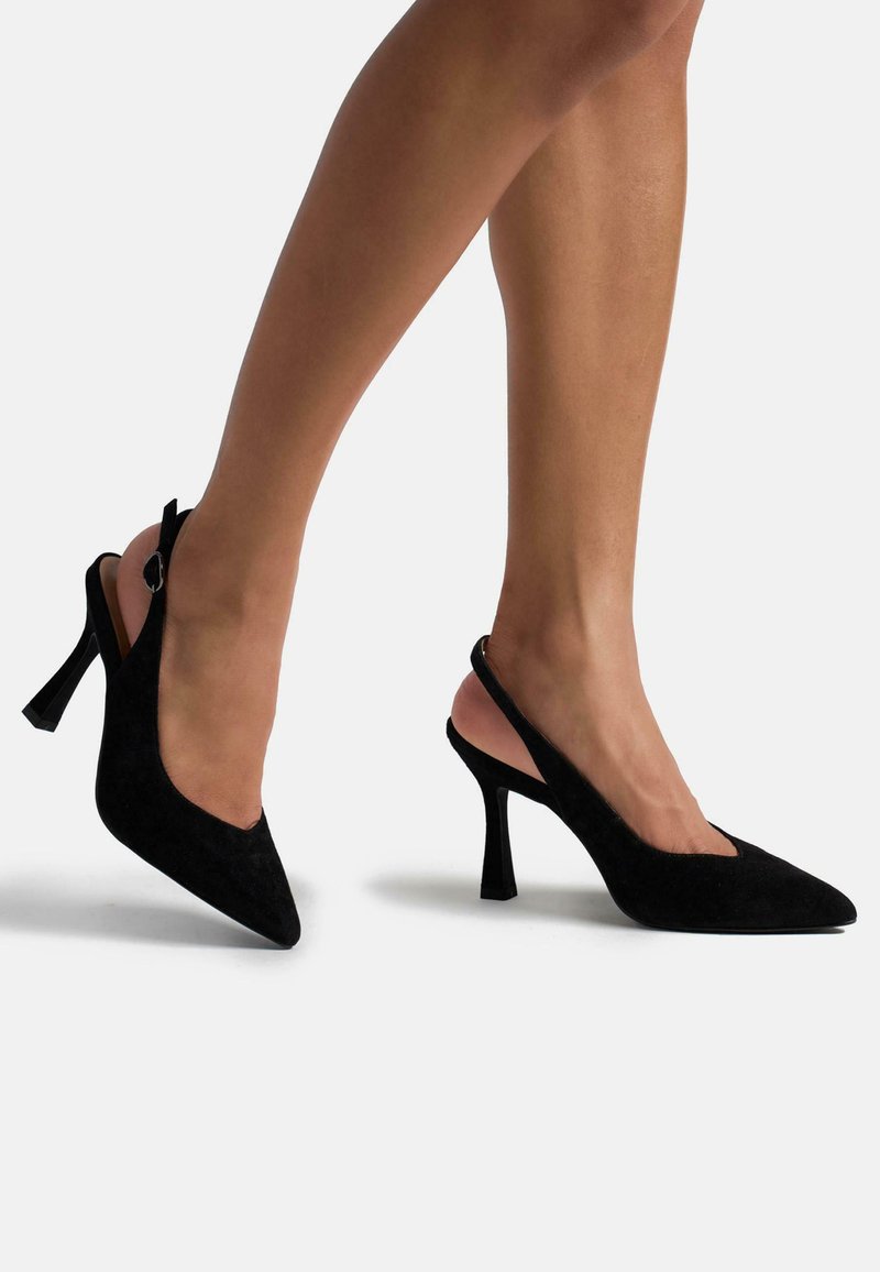Schwarze Wildleder-Slingback-Pumps mit spitzem Zehenbereich, dünnem Absatz und verstellbarem Riemen. Glatte Textur und minimalistisches Design mit profilierter Silhouette.
