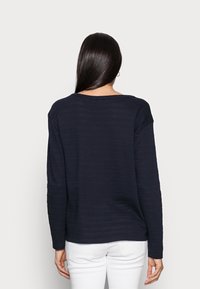 Marineblauw longsleeve shirt met een geribbelde textuur, ronde halslijn en verlaagde schouders, gecombineerd met witte broeken.