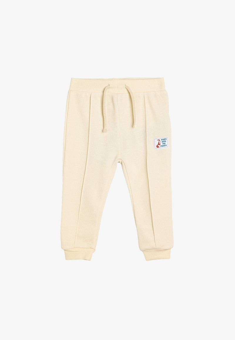 Cream-colored cotton sweatpants with a ribbed texture, drawstring waistband, tapered cuffs, and a side patch featuring a fox design.