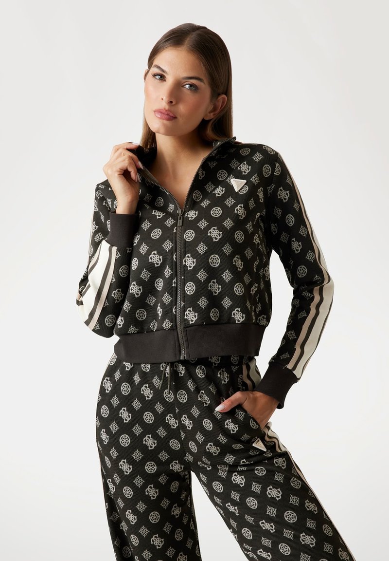 Black zip-up jacket with white geometric patterns, ribbed cuffs, and matching pants. Features vertical white stripes along sleeves.