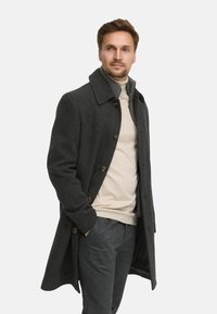 Dunkelgrauer Wollmantel mit Knopfverschluss, großem Kragen und Seitentaschen, getragen über einem hellbeigen Pullover und dunkelgrauen Hosen.