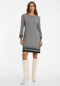 Schwarz-weißen Hahnentrittmuster Kleid mit langen Ärmeln, dekorativen schwarz-weißen gemusterten Manschetten und einem Saumakzent. Tragen mit weißen knielangen Stiefeln.