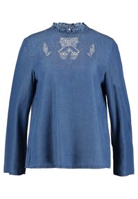 Chemise en denim à manches longues bleu foncé avec un col à volants et un détail en dentelle brodée de fleurs à l'avant. Coupe décontractée avec fentes sur les côtés.