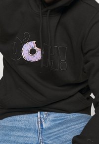 Černá mikina s kapucí, na které je grafika fialového donut s barevnými posypkami a textem "O' H!" v tučných písmenech. Měkká tkanina a volný střih.