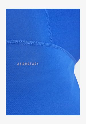 AeroReady anyagú tank top élénk kék színben, sima textúrával, lapos varratokkal és látható logóval az oldalon.