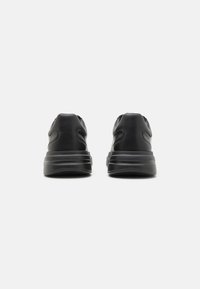 Zapatos deportivos negros con parte superior sintética suave, forma redondeada, suela gruesa y detalles de costura sutiles. Sin marcas visibles.