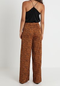 Oranssi ja musta leopardikuvioinen leveälahkeinen housut, valmistettu pehmeästä kankaasta. Sisältää korkeavyötäröisen muotoilun ja löysän istuvuuden.