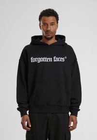 Sweatshirt à capuche noir en tissu doux. Il comporte une poche avant et un texte graphique blanc "visages oubliés" en caractères gras.