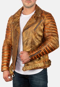 Giacca da motociclista in pelle dorata con accenti arancioni, pannelli trapuntati sulle spalle, tasche con cerniera e chiusura a fibbia in vita.