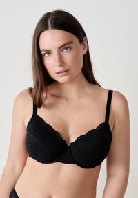 Bra nero in tessuto testurizzato con motivi geometrici, bordi in pizzo, spalline regolabili e finitura liscia.