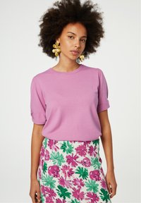 Roze T-shirt met korte mouwen en opgerolde mouwen, gecombineerd met een witte rok met bloemenprint met groene en roze bladeren en bloemen.