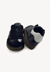 Mustat ja laivansiniset lenkkarit, joissa on mokkaa ja teksturoitua nahkaa, pyöreä kärki, nauhaknus, sekä kontrastivärinen harmaa kantatuki, jossa on teksturoitu pohja.