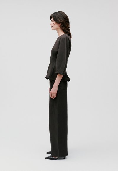 Schwarzes, tailliertes Oberteil mit Dreiviertelärmeln, kombiniert mit hochtaillierten, weiten Hosen. Glatte Textur, minimalistisches Design.