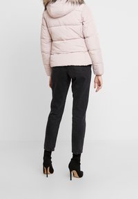 Svetle růžová nadýchaná bunda s kapucí a umělým kožíškem, ve spojení s černými elastickými úzkými džínami a černými kotníkovými botami na podpatku.