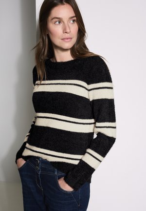 Pull rayé noir et crème avec une texture duveteuse et un décolleté rond. Les rayures varient en largeur, associé à un jean bleu foncé.