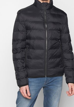 Black puffer jacket with a high collar, horizontal quilted pattern, front zipper, and side pockets, worn over blue jeans.