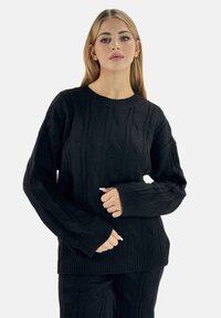 Maglione nero a maglia con scollo rotondo, maniche lunghe e polsini a costine. Texture morbida con intricate fantasie in rilievo su tutta la stoffa.