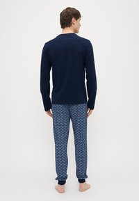 Camiseta de manga larga azul marino con cuello redondo combinada con pantalones de pijama estampados con diseños en azul y blanco. Tejido suave y ligero.