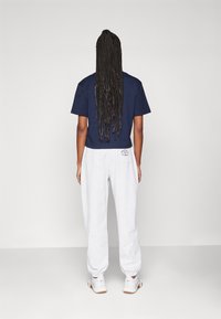 Marinblå, kortärmad t-shirt, grå sweatpants med uppvikta anklar och vita sneakers. Långt flätat hår synligt bakifrån. Enkelt, avslappnat outfit.